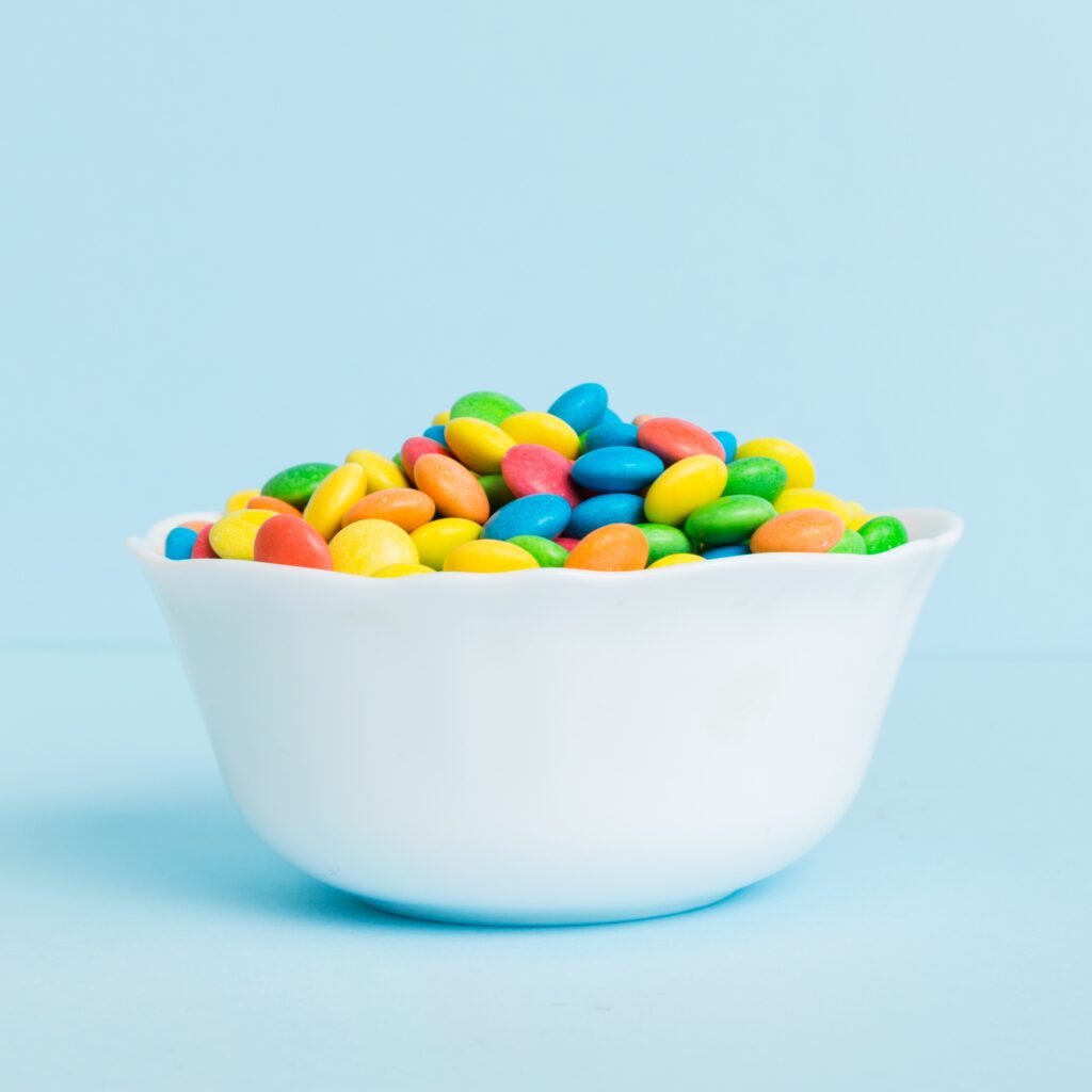 Multicolored candies in a bowl on a colored background. birthday and holiday concept. Top view with copy space.